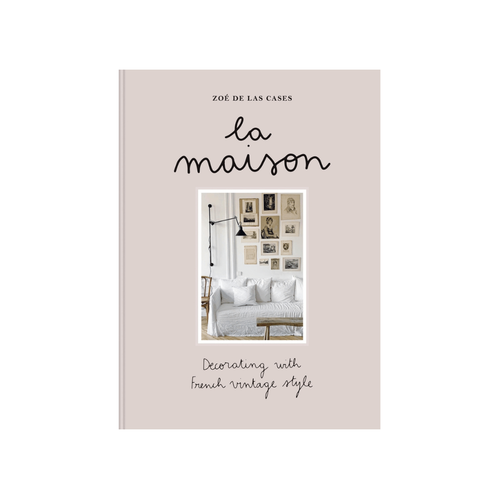 La Maison by Zoé de Las Cases, featuring French vintage style and interior inspiration. The book cover featuring a soft, oatmeal-coloured background with a central photograph of a lived-in, soulful living space. A white linen sofa sits beneath a gallery wall of vintage sketches and portraits, illuminated by a slender black industrial-style wall lamp.
