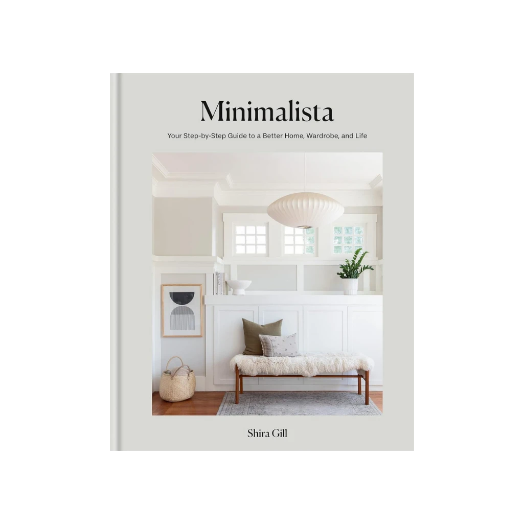Minimalista by Shira Gill, practical decluttering for a mindful and intentional home. Book cover featuring a serene, sun-drenched entryway. The scene is composed of soft whites and woods, with a woven basket, a sheepskin-covered bench, and a delicate paper lantern hanging from the ceiling.