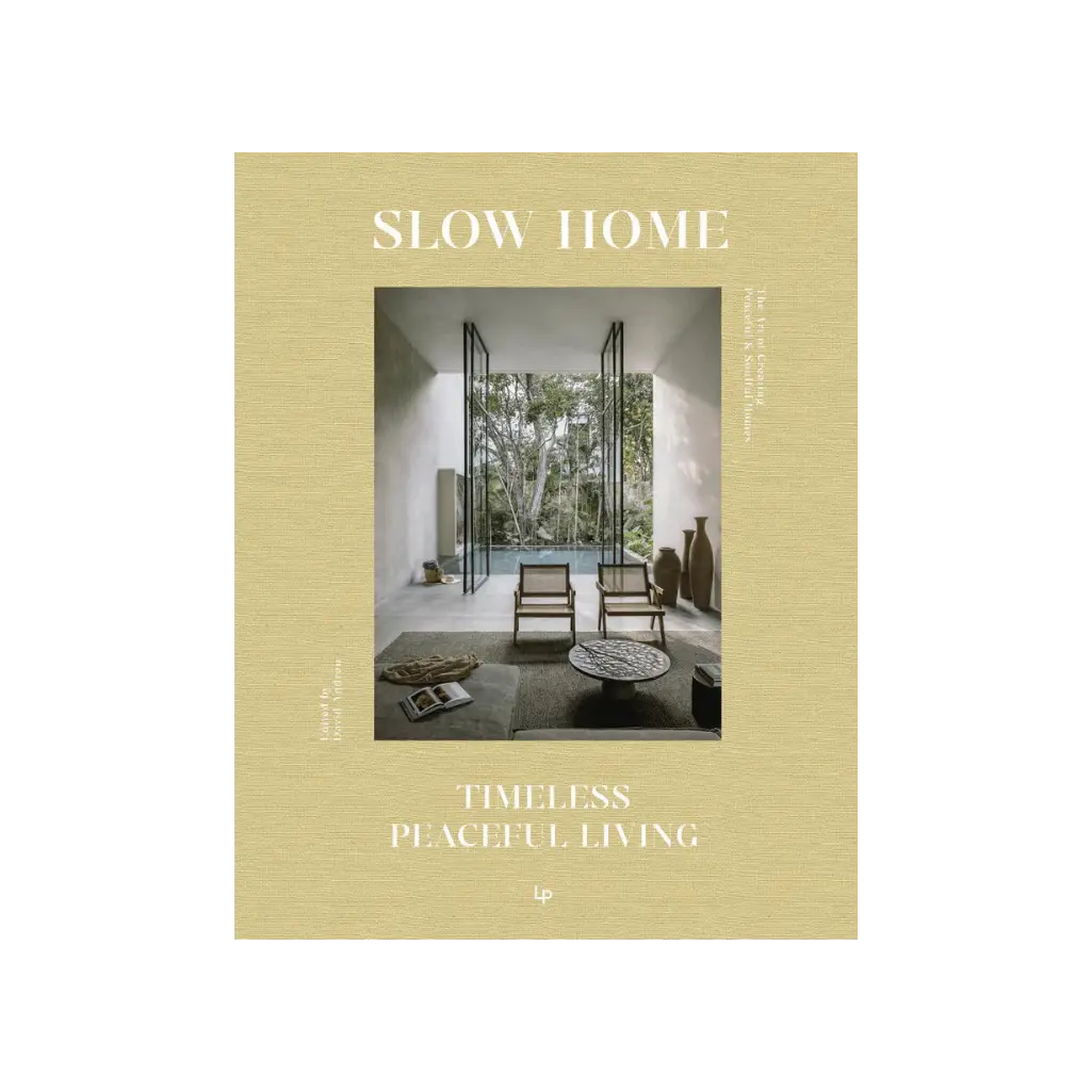 Slow Home by Daniela Santos, celebrating timeless and peaceful living in a restored home. Book cover showing a minimalist indoor-outdoor living space with warm, earthy tones, featuring two woven chairs facing a lush green garden and a tranquil pool.