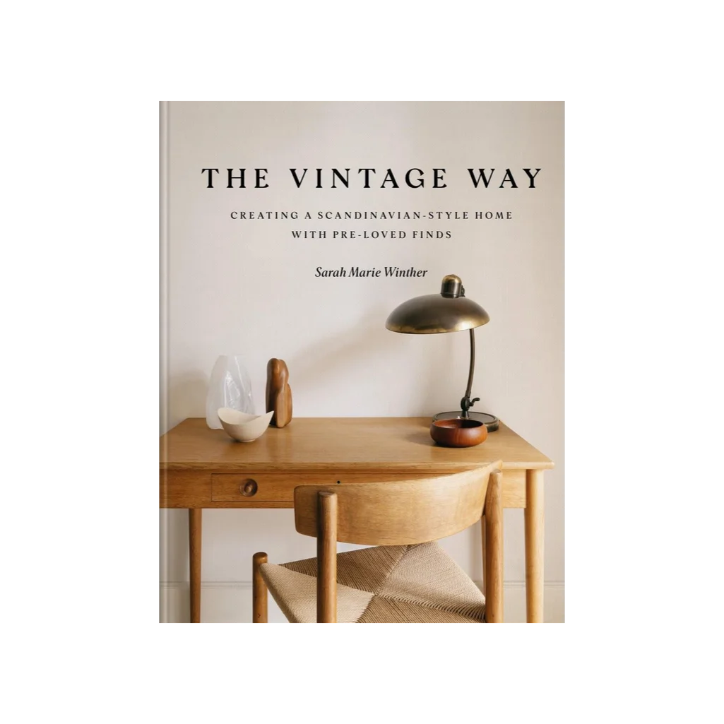 The Vintage Way by Sarah Marie Winther, a guide to creating a soulful, vintage-inspired home. Book cover featuring a simple wooden desk is set against a pale wall, adorned with a mid-century brass lamp and a few hand-carved objects, celebrating the beauty of pre-loved Scandinavian design.