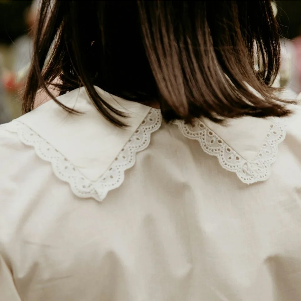 A close-up of a child wearing a cream-coloured blouse with a delicate embroidered lace collar, highlighting heirloom quality.
